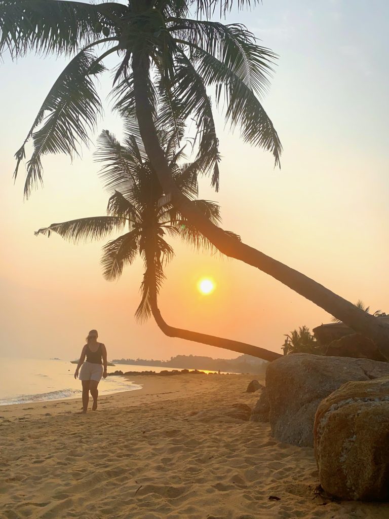 Marianne alleine am Strand mit Palmen entlang laufend zum Sonnenuntergang (Thailand)