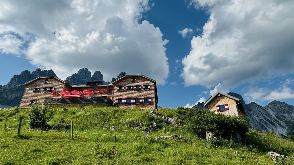 Hofpürglhütte vor leicht bewölktem Himmel, im Hintergrund Große Bischofsmütze (Alpen)