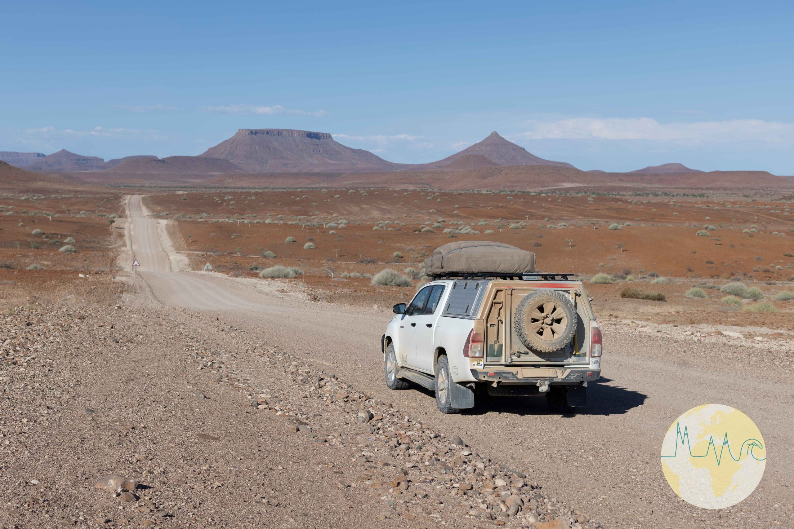 Toyota Hillux mit Dachzelt auf einer Schotterstraße stehend, im Vordergrund karges Land, im Hintergrund Berge