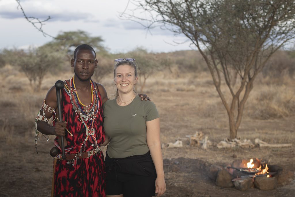 Marianne mit dem Masai Michael gemeinsam neben einem Lagerfeuer stehend in Kenia