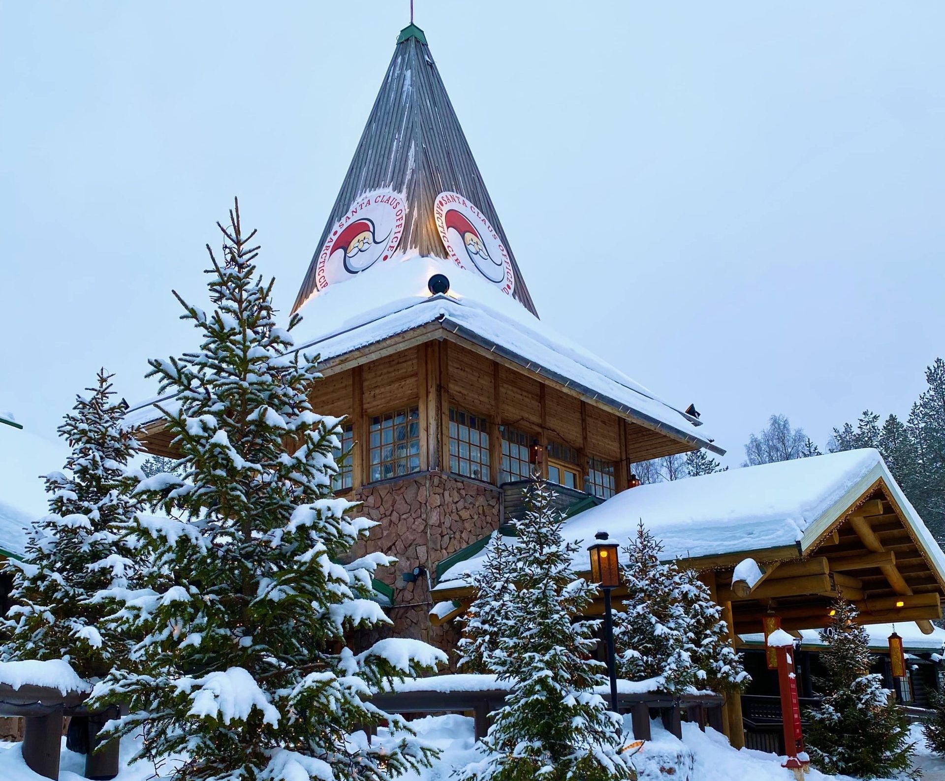 Holzhaus mit Spitzdach, davor verschneite Bäume im Santa Claus Village bei Rovaniemi in Finnland