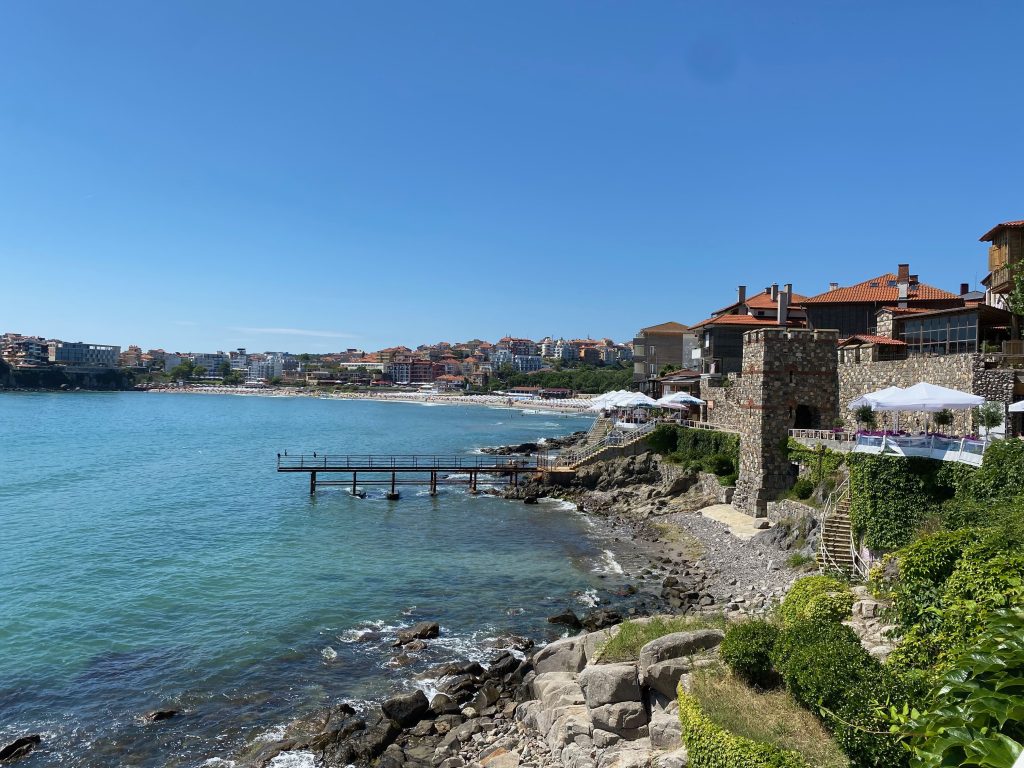 Blick auf die Küste von Sosopol an der Schwarzmeerküste in Bulgarien - ins Meer reichender Steg, dahinter Steinhäuser, im Hintergrund Strand