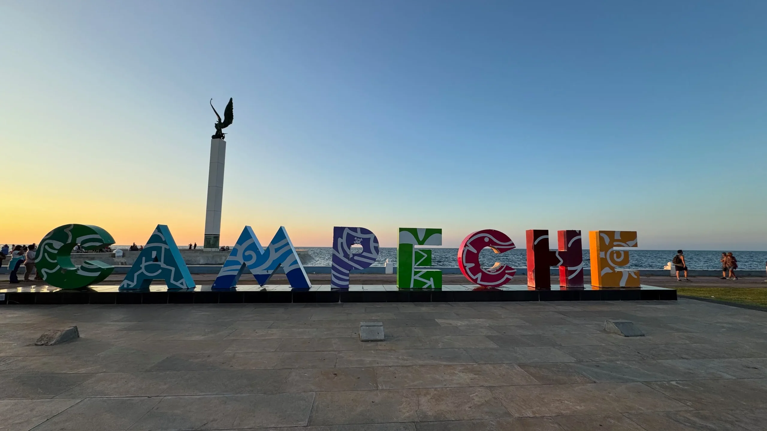 Bunte Buchstaben zum Schriftzug Campeche am Meer, im Hintergrund das Meer und ein Sonnenuntergang