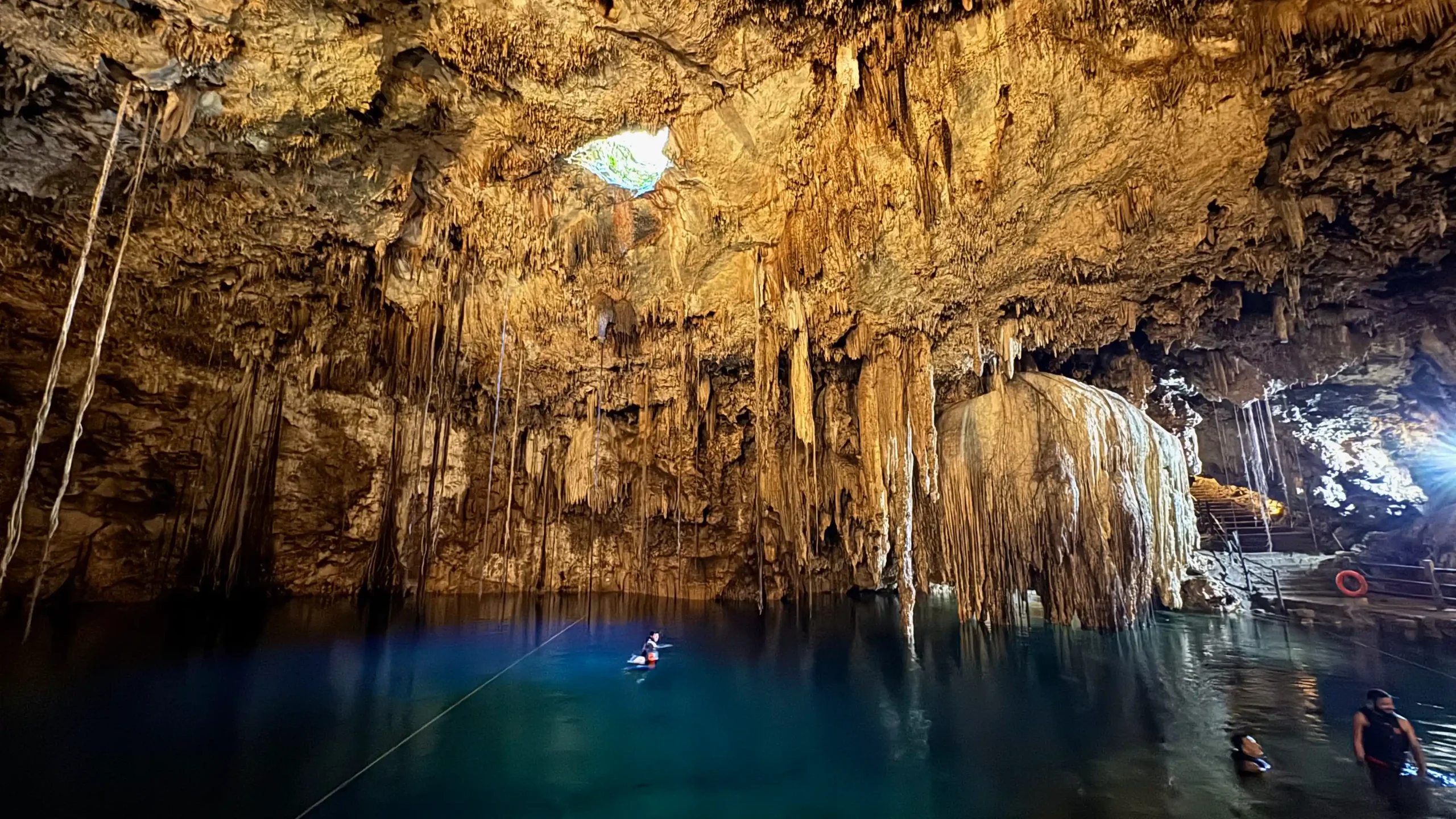 Höhle der Cenote Xkeken in Mexiko mit einem Loch nach oben und tiefblauem Wasser, in dem einige Menschen schwimmen