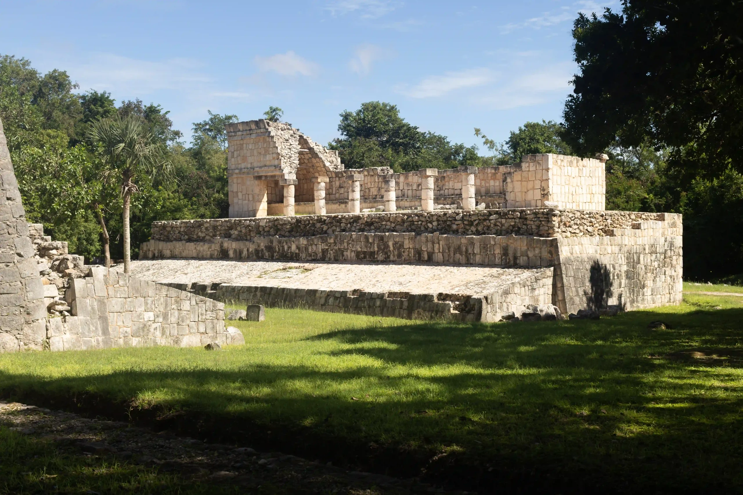 Auf einem Podest stehende Ruine mit großen Säulen von Chichén Itza, im Vordergrund grüne Wiese
