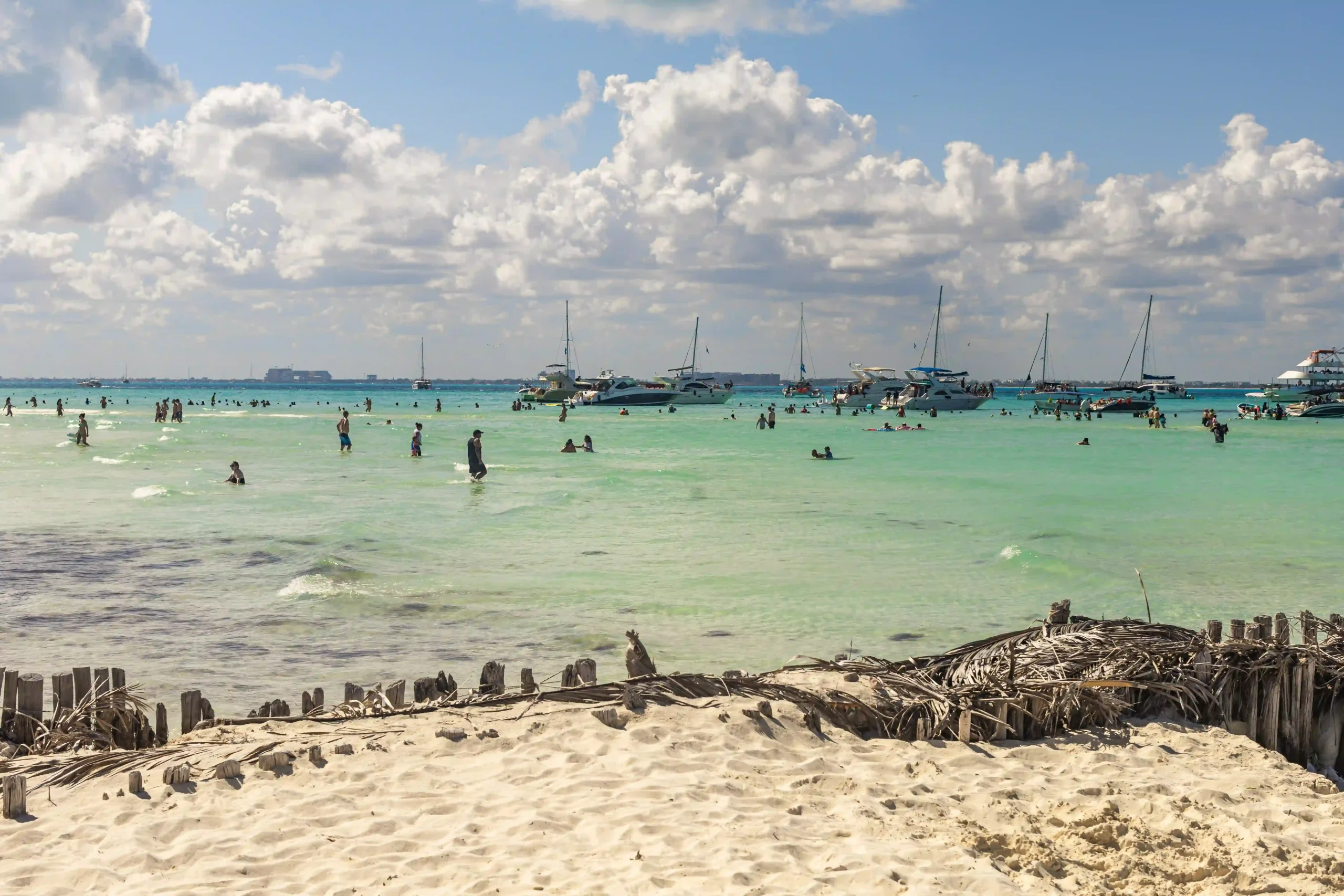 Zahlreiche Menschen im Wasser an der Playa Norte auf Isla Mujeres, im Hintergrund Yachten und ein paar Wolken