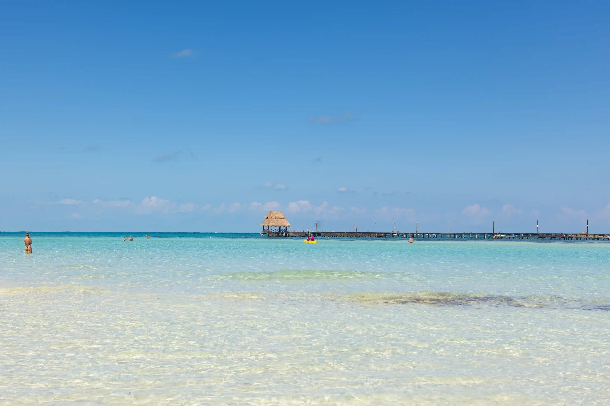 Sandstrand Playa Norte auf Isla Mujeres mit türkisblauem Meer, im Hintergrund ein Steg und einige Menschen im Wasser